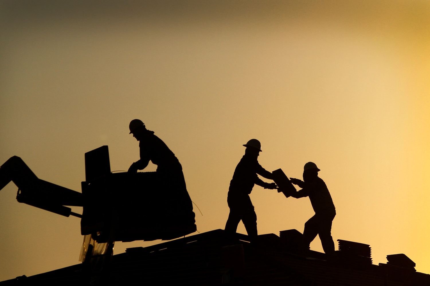 Workmen placing tiles on a house roof